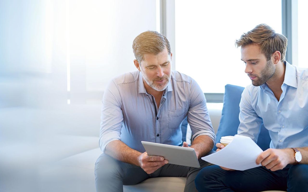 Mature businessman using a digital tablet to discuss information with a younger colleague in a modern business lounge